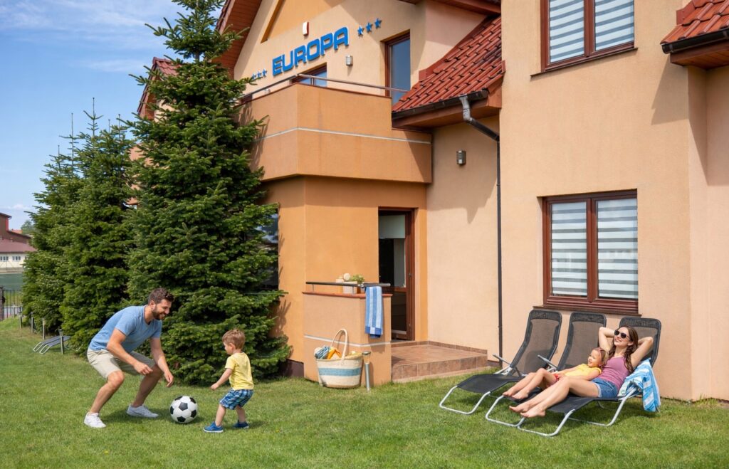 Eine Familie macht Sommerurlaub im Holiday House Europa in Rewal. Die Mutter liegt mit der Tochter auf den Sonnenliegen und der Vater spielt mit dem Sohn Fußball