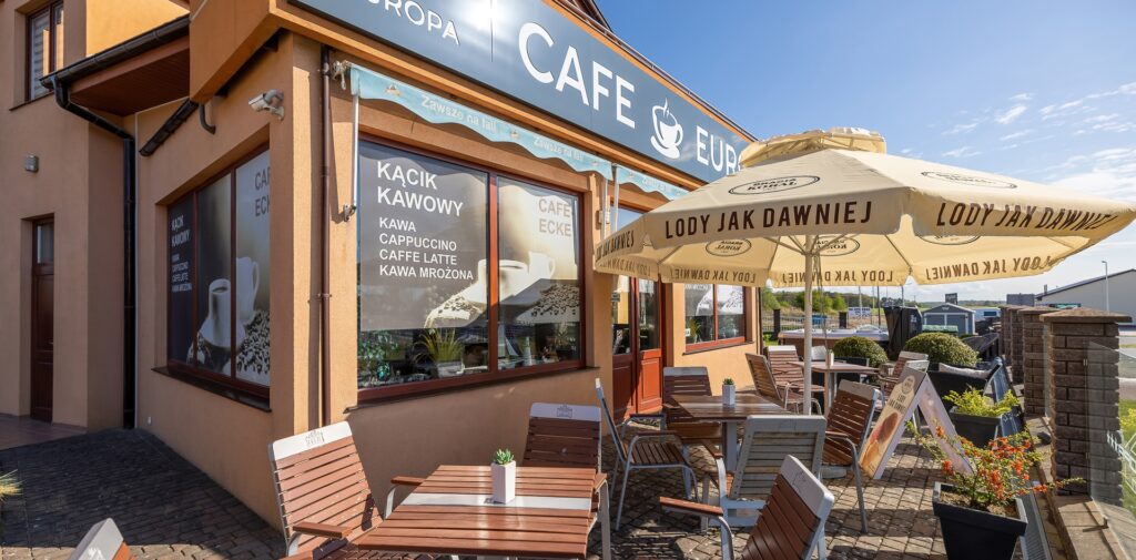 Cafe EUROPA mit Sonnenterrasse in Rewal. Vor dem Cafe stehen mehrere Tische mit Stühlen und Sonnenschirmen.
